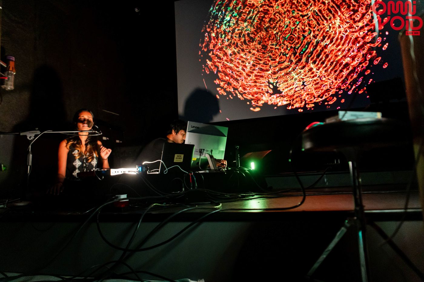 Sahitya and Harsh performing under a projected red-and-blue cymatics pattern.