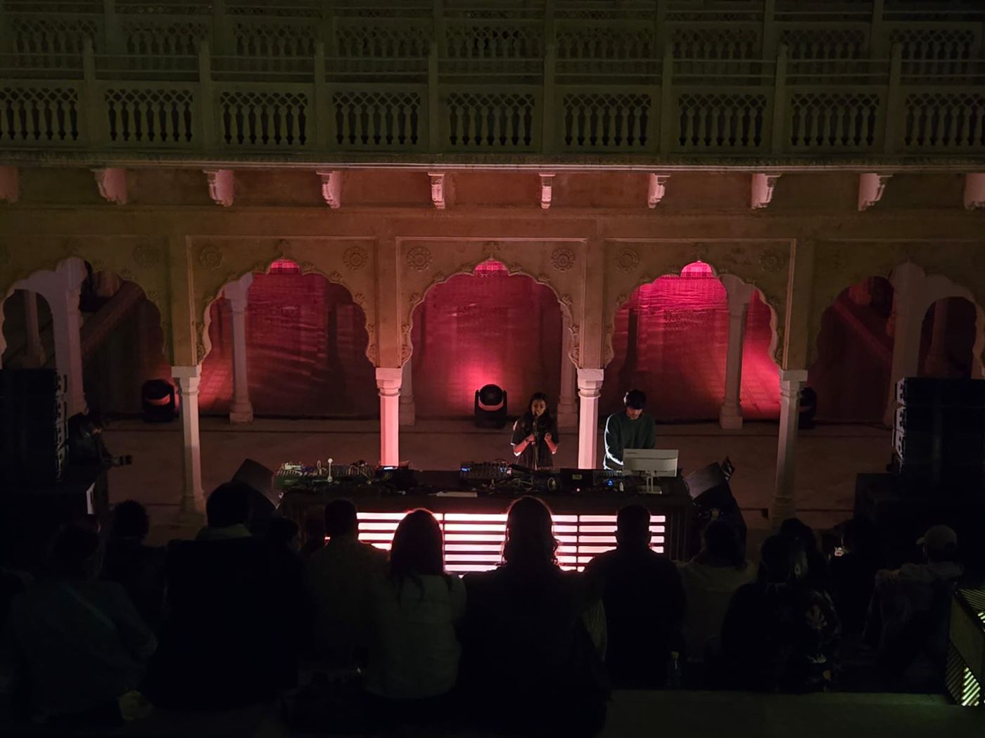 A pause.dxa set in a palace courtyard under pink-lit arches, audience in silhouette.