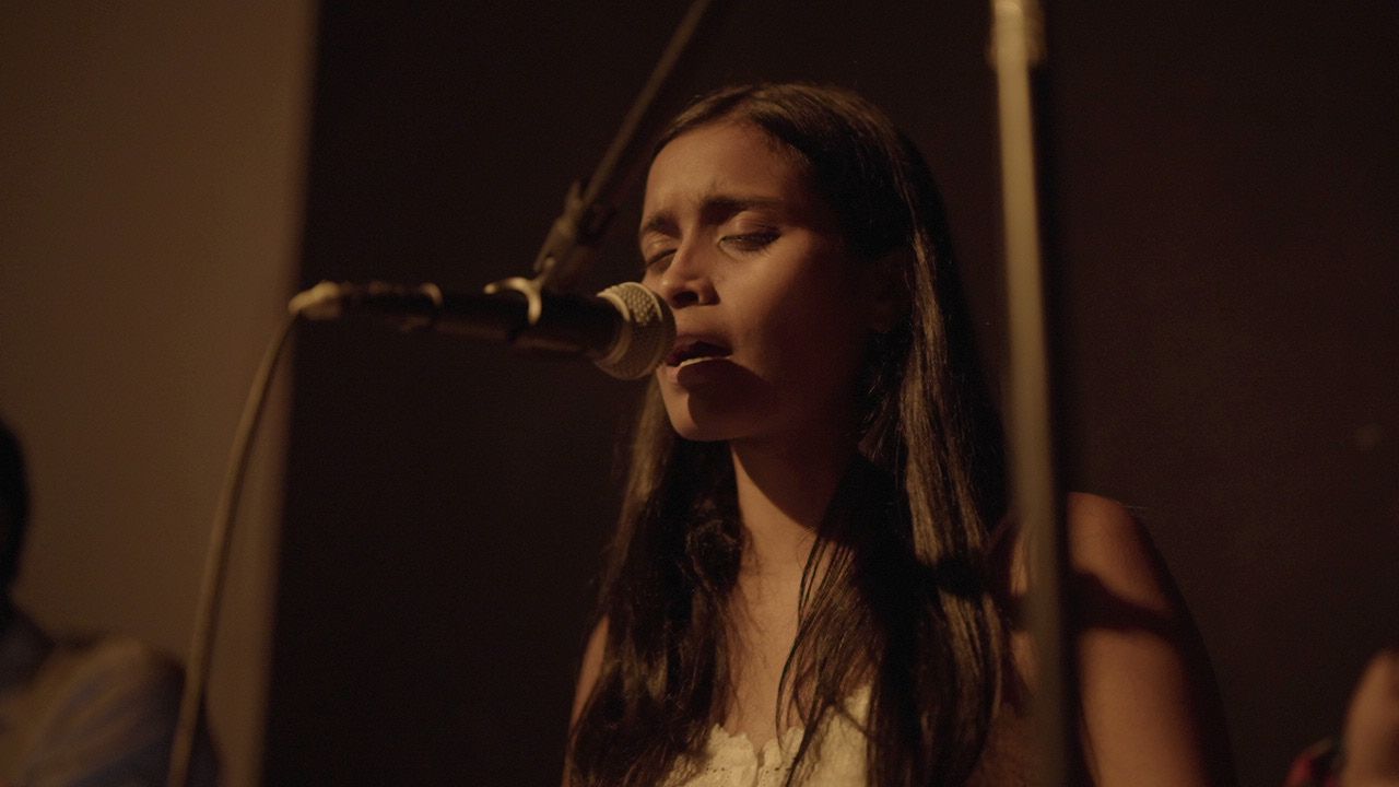 Sahitya singing into a microphone, eyes closed.