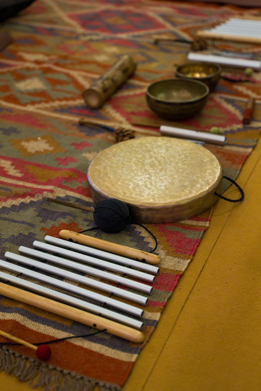 Singing bowls, a frame drum and chimes laid out on a rug.
