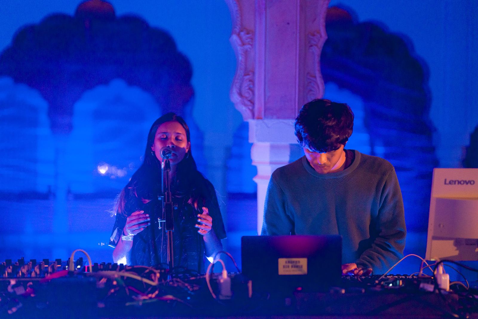 Sahitya singing and Harsh at the synths under deep-blue light in the stepwell arches at Magnetic Fields Nomads 2026.